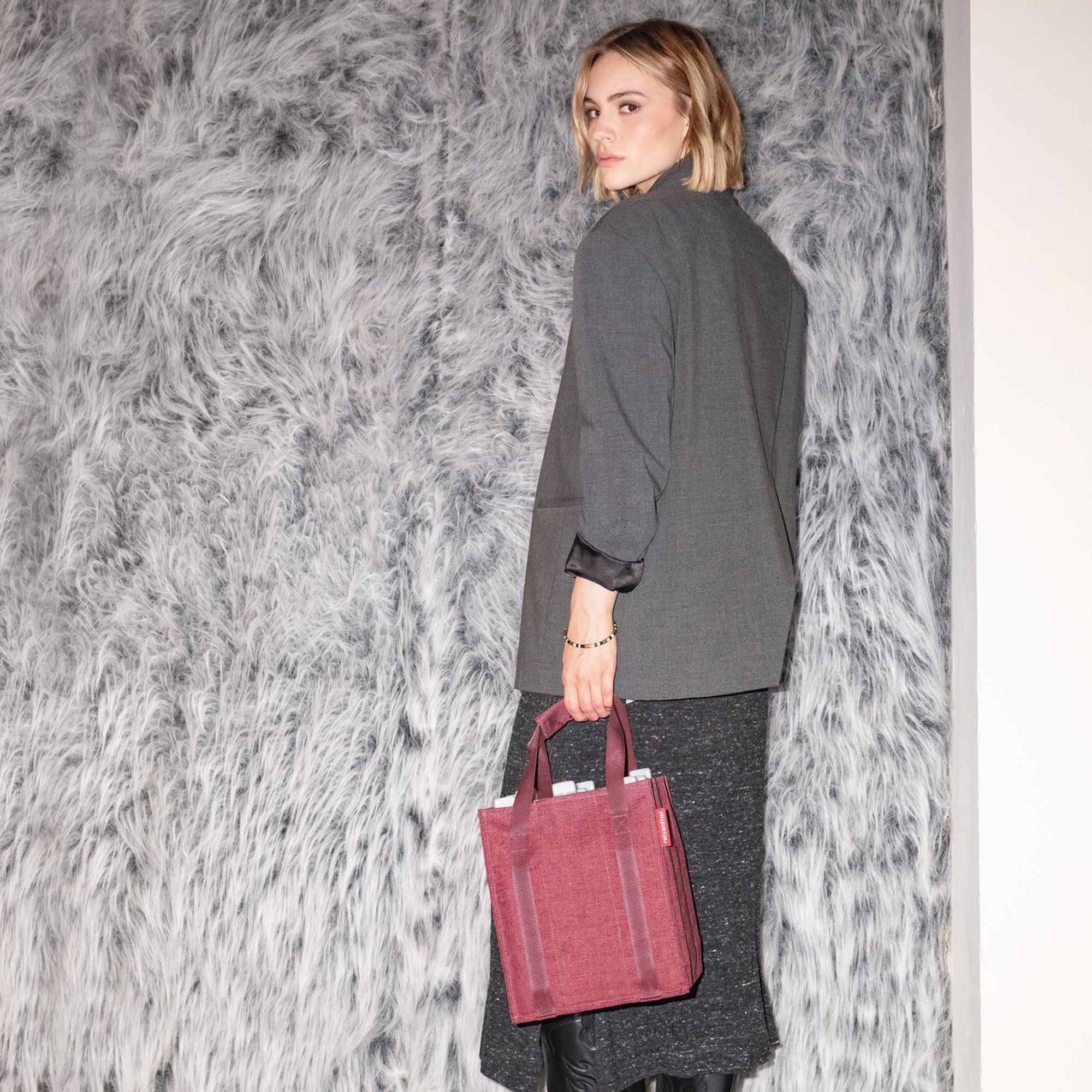 Woman with burgundy handbag in front of fur wall