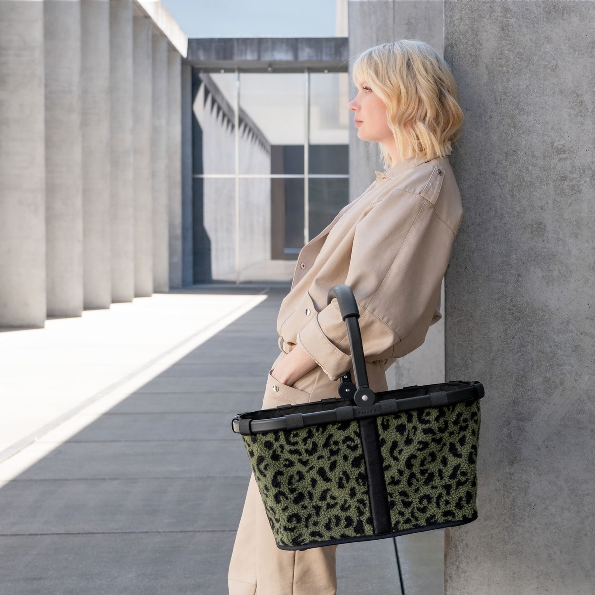 Woman leaning on wall holding green leopard print shopping b