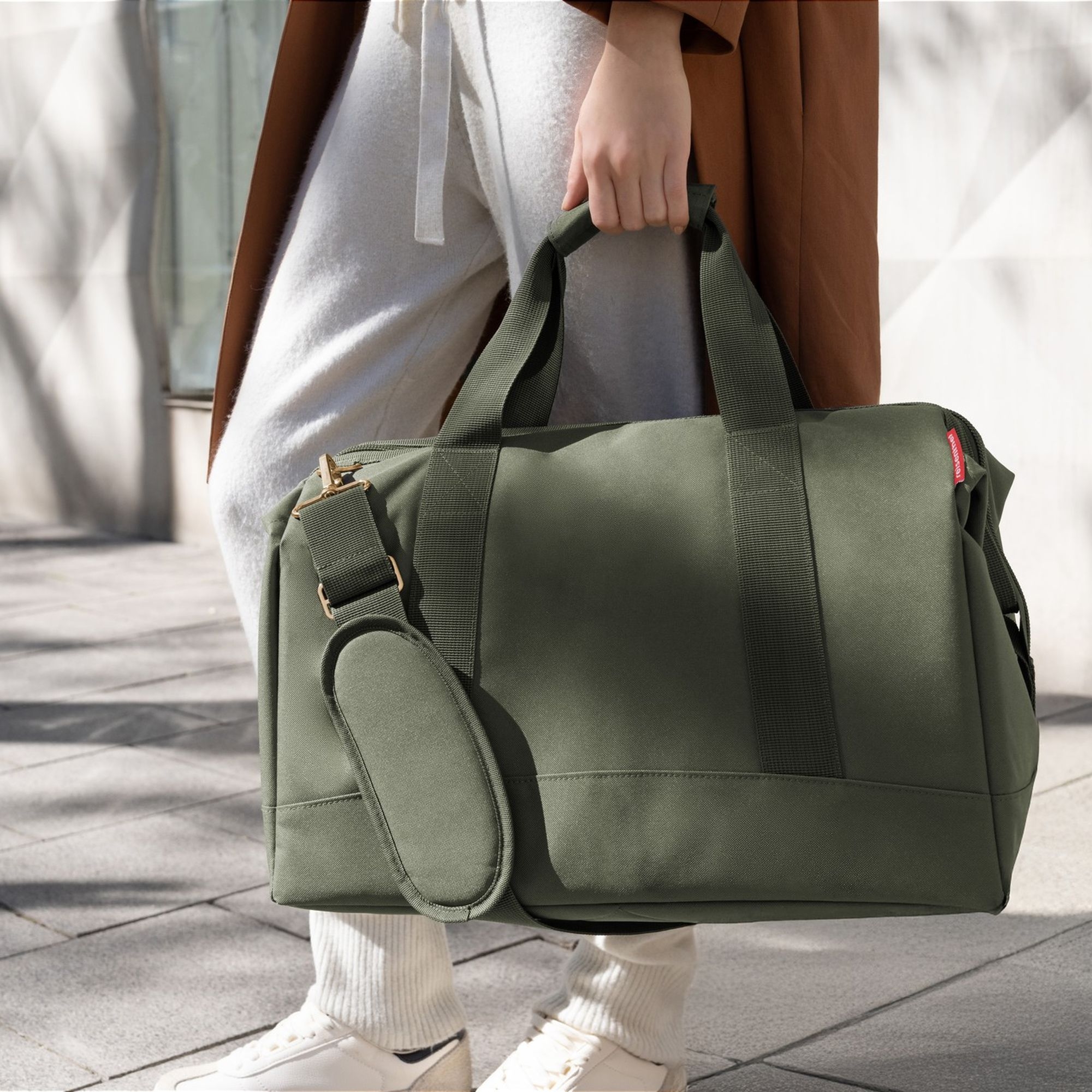 Person carrying large olive green travel bag by handle
