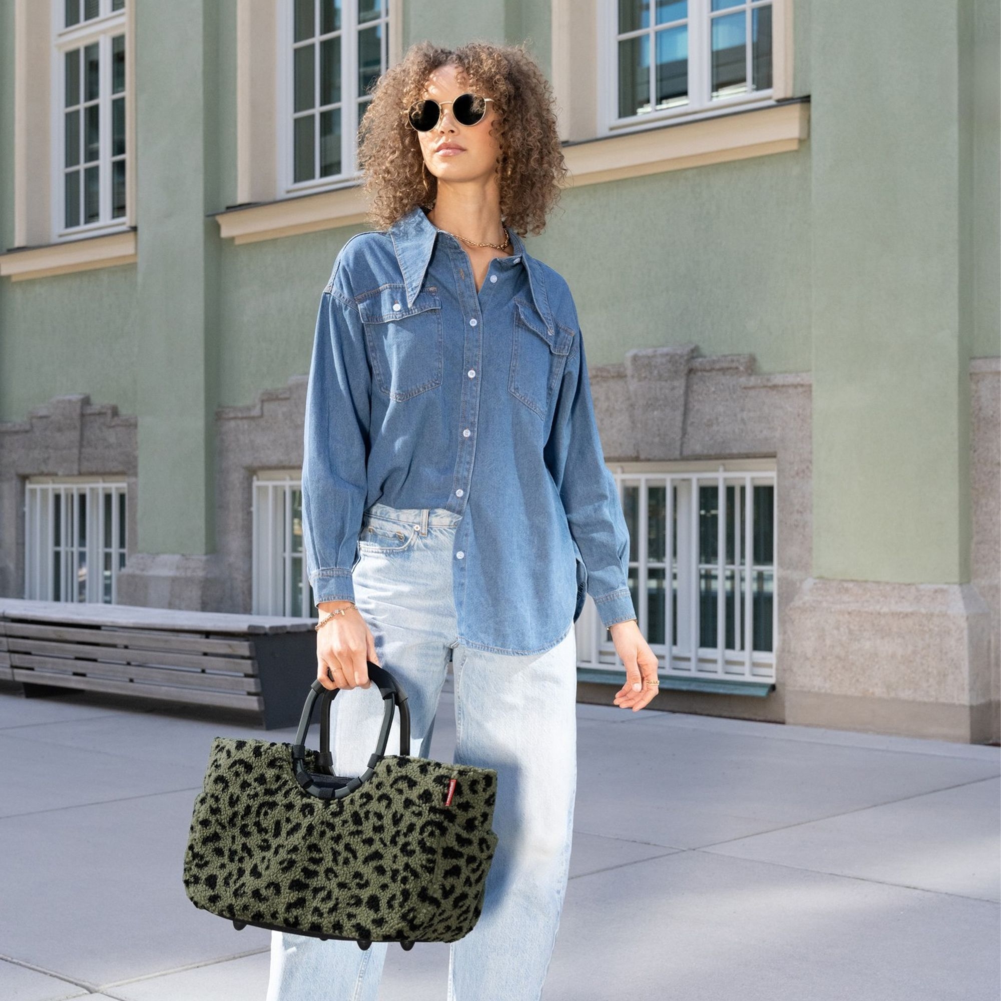 Woman wearing denim shirt and green leopard print bag